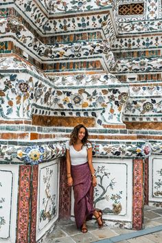 a woman standing in front of a wall with colorful tiles and flowers on the walls