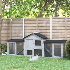 a white rabbit sitting in the grass next to a wooden fence with a house on top