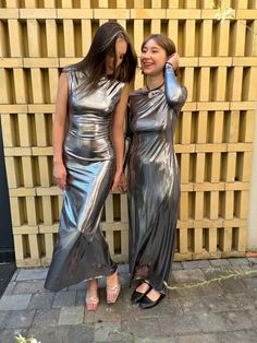 two women standing next to each other in silver dresses and one is talking on the phone