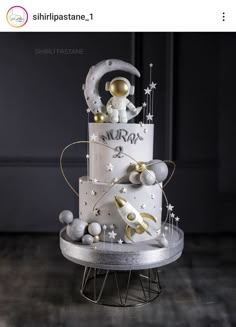 a three tiered cake with an astronaut on the top and stars around it, sitting on a metal stand