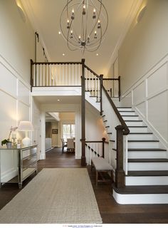 a large hallway with stairs and chandelier in the center, along with a rug on the floor