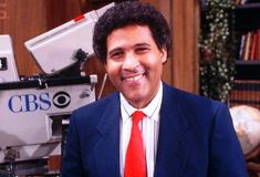 a man in a suit and red tie standing next to a camera on a television set