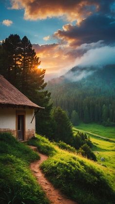 a small hut in the middle of a grassy field with trees and mountains in the background