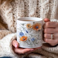 a woman is holding a coffee mug with flowers painted on the outside and inside it