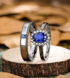 two wedding rings with blue sapphire stones on top of each other in front of a tree stump