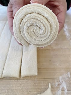 a person is holding a rolled up pastry on a wooden surface with flour sprinkled around it