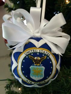 an ornament hanging from a christmas tree decorated with white ribbon and the seal of the united states air force