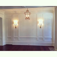 an empty room with two lamps on the wall and hard wood floors in front of it