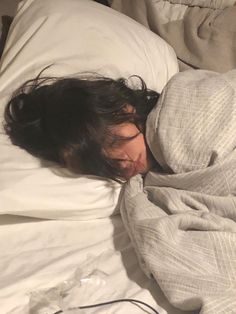 a woman sleeping in bed with her head on the pillow and eyes closed, covered by a blanket