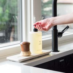 a person's hand holding a soap dispenser next to a window