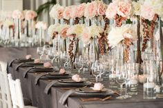 the table is set with many tall vases filled with flowers