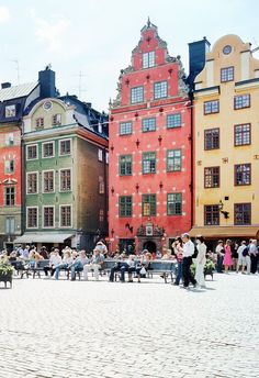 many people are sitting on benches in the middle of a city square with tall buildings