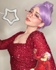 a woman with purple hair and glasses is wearing a red sequin dress, holding a star shaped object in her right hand