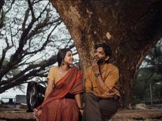 a man and woman sitting next to each other under a tree