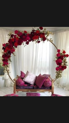 a couch covered in lots of pink and red pillows next to a white curtained window