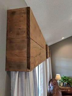 a brown couch sitting under a window next to a wooden box hanging from the ceiling