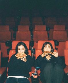 two women sitting in an auditorium eating pizza