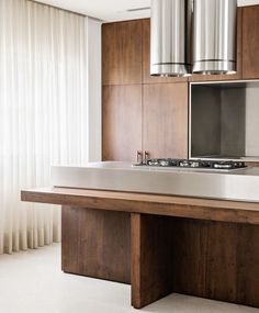 a modern kitchen with stainless steel appliances and wood cabinetry, along with white curtains