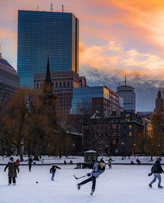 people are playing in the snow on a sunny day with tall buildings behind them and pink sky