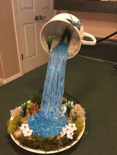 a cup with water pouring out of it on top of a plate covered in moss