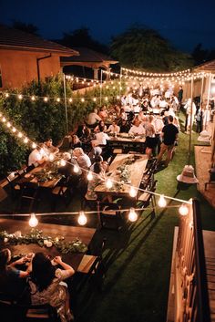 an outdoor dining area with string lights and people sitting at tables eating food on the grass