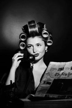 a woman with curls on her hair is talking on the phone and holding a newspaper