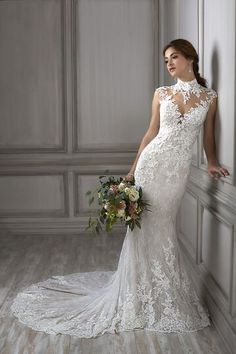 a woman in a white wedding dress standing next to a wall holding a flower bouquet