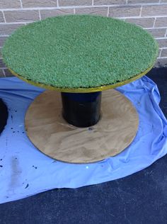 a table with grass on top sitting in front of a brick wall and blue tarp