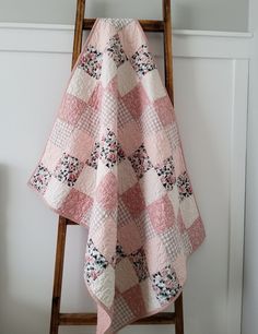 a pink and white quilt sitting on top of a wooden chair next to a wall