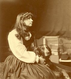 an old black and white photo of a woman sitting next to a dog