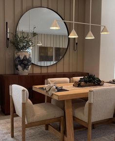 a dining room table with four chairs and a round mirror