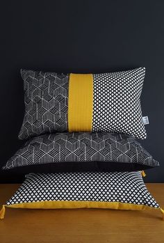 three black and white pillows stacked on top of each other with yellow trimmings