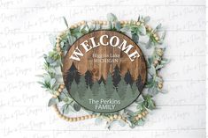 a wooden welcome sign hanging from the side of a wall with leaves and berries around it