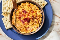 a blue plate topped with a bowl of macaroni and cheese next to crackers