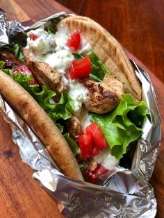 a taco filled with meat, lettuce and tomatoes on top of aluminum foil