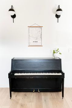 a black piano sitting on top of a hard wood floor next to two wall lights