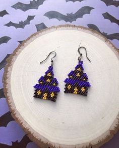 a pair of beaded triangle earrings sitting on top of a piece of tree stump