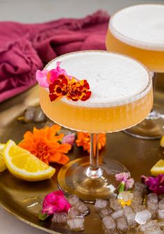 two cocktails on a tray with flowers and ice