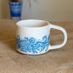 a blue and white coffee cup sitting on top of a table next to a vase