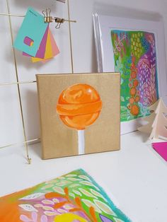 there are paintings on the table and one has an orange lollipop