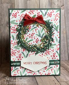 a christmas card with a wreath and red bow on it, sitting on a wooden surface