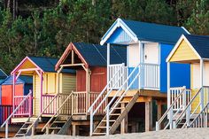 colorful beach huts lined up on the sand with stairs leading to them and trees in the background