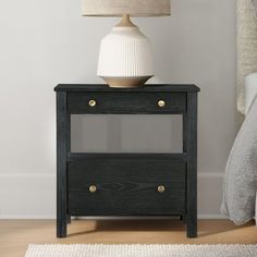 a black night stand with two drawers and a white lamp next to it on a wooden floor