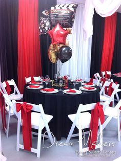 a black table topped with white chairs and red napkins next to a tall balloon