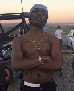 a shirtless man with his arms crossed standing in front of a truck at sunset