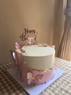 a birthday cake with pink and gold butterflies on it sitting on a checkered table cloth