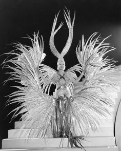 a black and white photo of a woman with feathers on her head, standing in front of a mirror