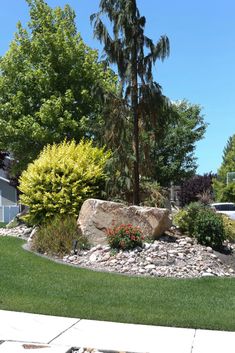 a large rock sitting in the middle of a lush green yard next to a tree