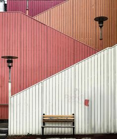 a wooden bench sitting in front of a tall building with red and white panels on it