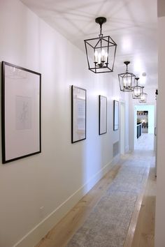 an empty hallway with pictures hanging on the wall and light fixtures in front of it